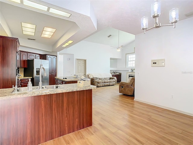 kitchen featuring ceiling fan with notable chandelier, a sink, stainless steel refrigerator with ice dispenser, light wood finished floors, and decorative light fixtures