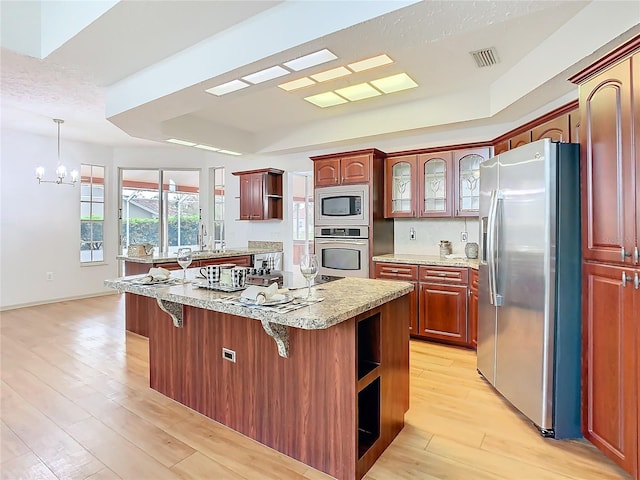 kitchen with a tray ceiling, open shelves, stainless steel appliances, visible vents, and light wood-type flooring