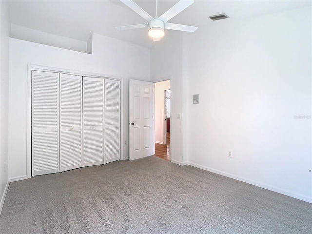 unfurnished bedroom with baseboards, visible vents, a towering ceiling, carpet flooring, and a closet