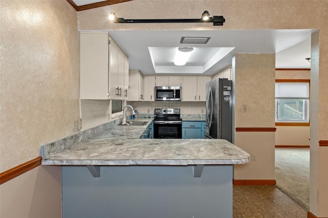 kitchen with light countertops, appliances with stainless steel finishes, a peninsula, a raised ceiling, and a sink