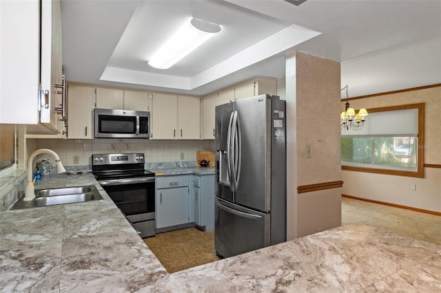 kitchen featuring backsplash, light countertops, appliances with stainless steel finishes, a raised ceiling, and a sink