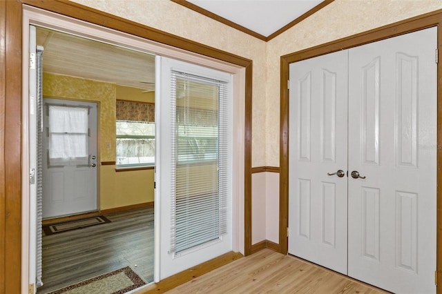 doorway featuring baseboards, visible vents, wallpapered walls, crown molding, and light wood-type flooring