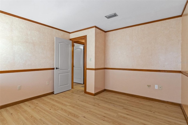 empty room with baseboards, visible vents, light wood-type flooring, and ornamental molding