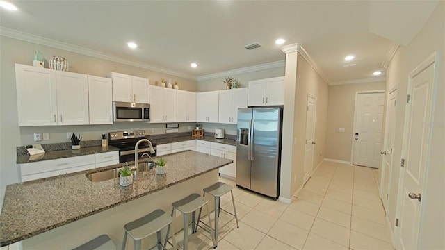 kitchen with white cabinets, light tile patterned floors, stainless steel appliances, a breakfast bar area, and ornamental molding