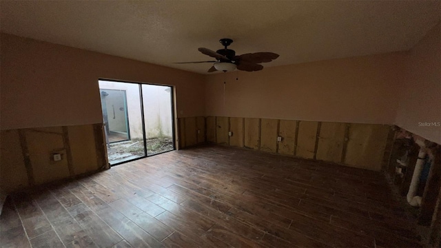 empty room featuring wood walls, dark wood-type flooring, and ceiling fan