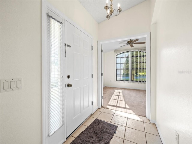 tiled foyer entrance featuring ceiling fan with notable chandelier, vaulted ceiling, and a healthy amount of sunlight