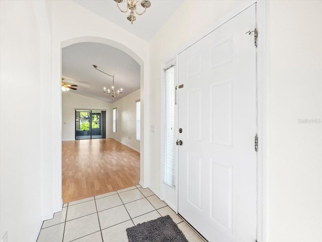 entrance foyer featuring ceiling fan with notable chandelier, light tile patterned flooring, and vaulted ceiling