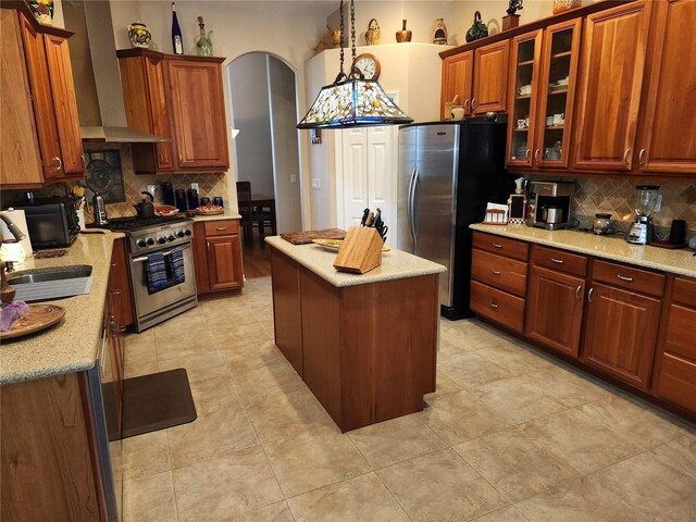 kitchen with backsplash, light stone counters, a center island, wall chimney exhaust hood, and appliances with stainless steel finishes