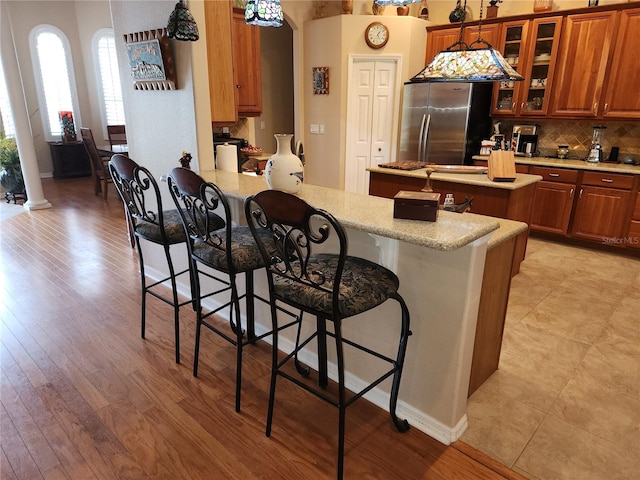 kitchen featuring stainless steel fridge, light hardwood / wood-style floors, a breakfast bar, kitchen peninsula, and decorative backsplash