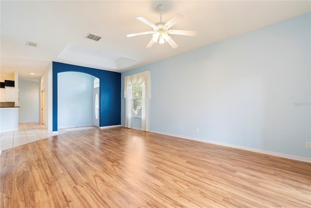 unfurnished living room featuring light wood-style floors, visible vents, arched walkways, and a ceiling fan