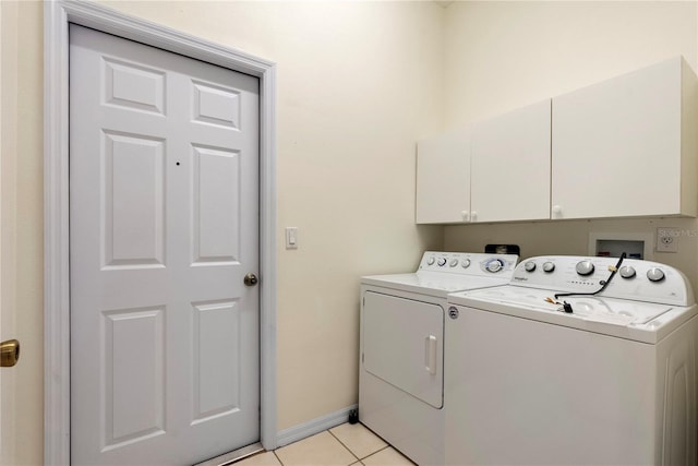 clothes washing area with light tile patterned floors, washer and clothes dryer, cabinet space, and baseboards