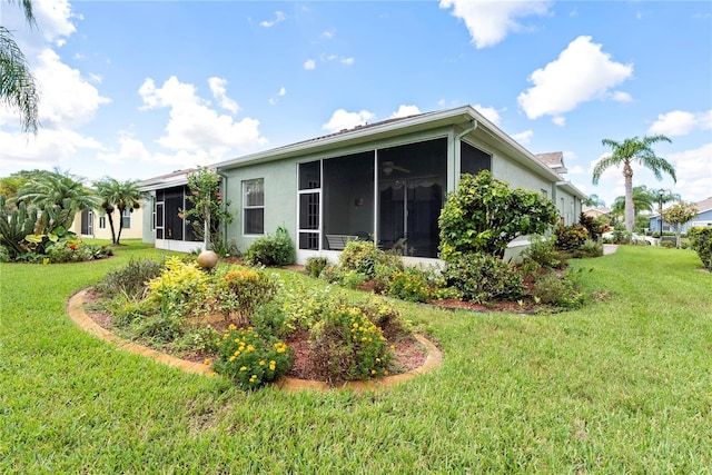 back of house featuring a garage, a yard, a sunroom, and stucco siding