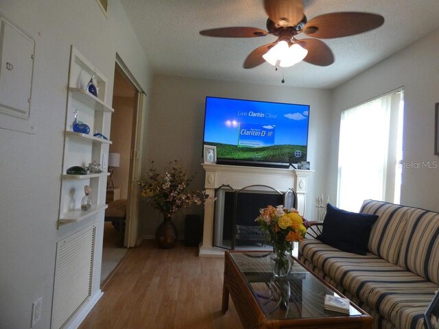 living room with a textured ceiling, light wood-type flooring, and ceiling fan