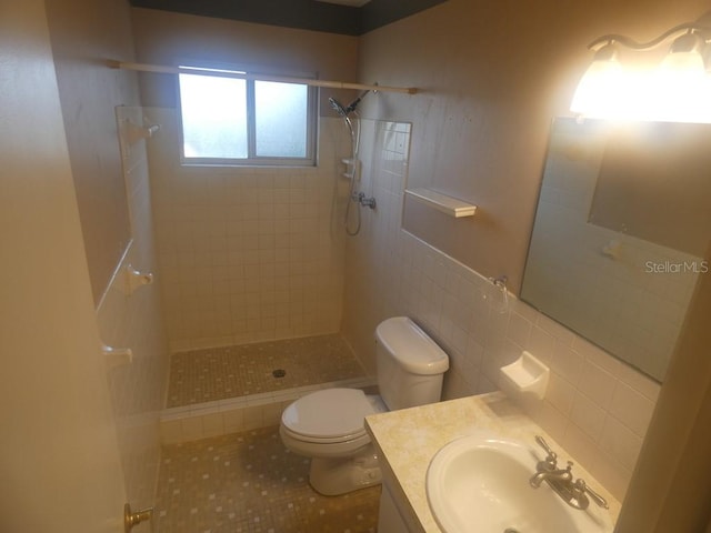 bathroom with a tile shower, tile patterned flooring, tile walls, and toilet