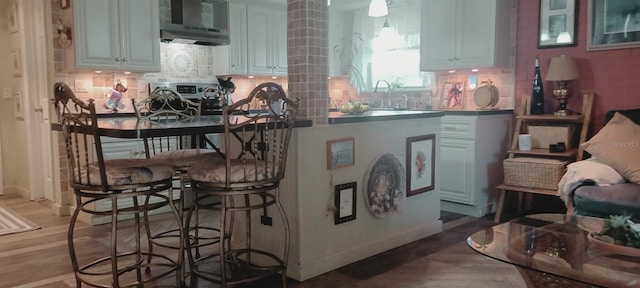 kitchen with white cabinetry, a breakfast bar, wall chimney range hood, and light wood-type flooring