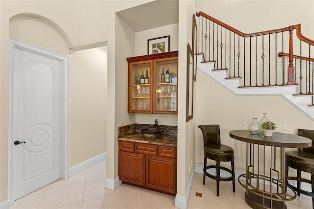 bar featuring light tile patterned floors, a sink, baseboards, stairs, and wet bar