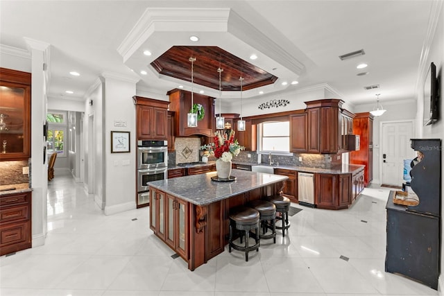 kitchen featuring a raised ceiling, appliances with stainless steel finishes, a healthy amount of sunlight, a kitchen island, and a sink