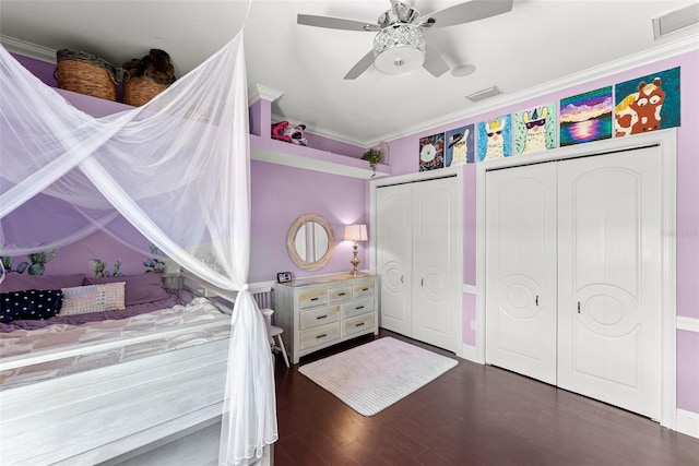 bedroom featuring crown molding, visible vents, two closets, and wood finished floors