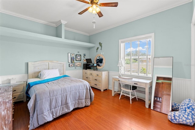 bedroom with a wainscoted wall, crown molding, a ceiling fan, and wood finished floors