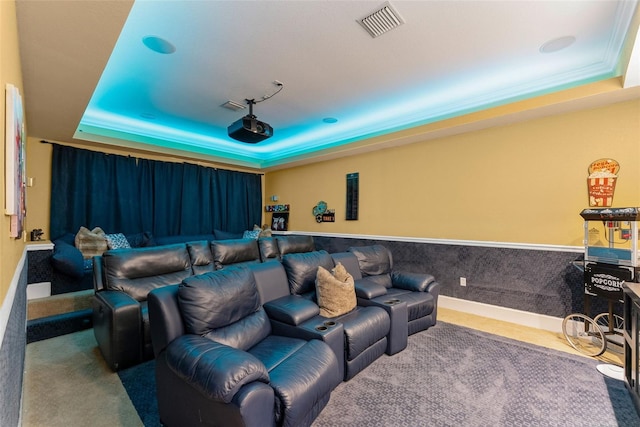 carpeted home theater room featuring visible vents, a tray ceiling, and wainscoting