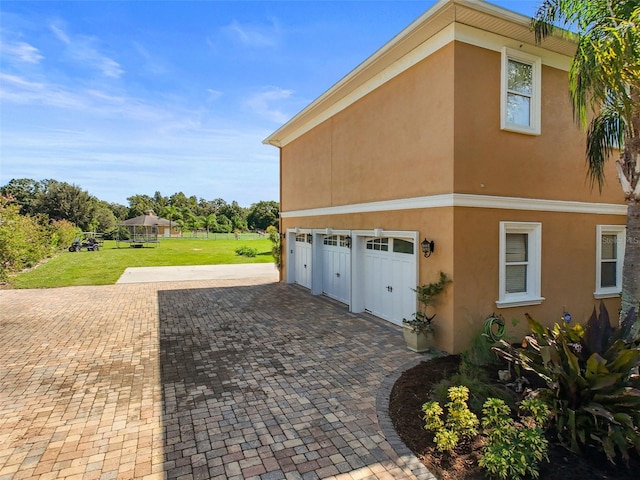 view of side of home with a garage, decorative driveway, a lawn, and stucco siding