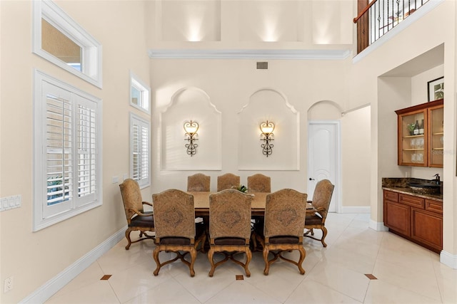 dining area featuring visible vents, light tile patterned flooring, a towering ceiling, and baseboards