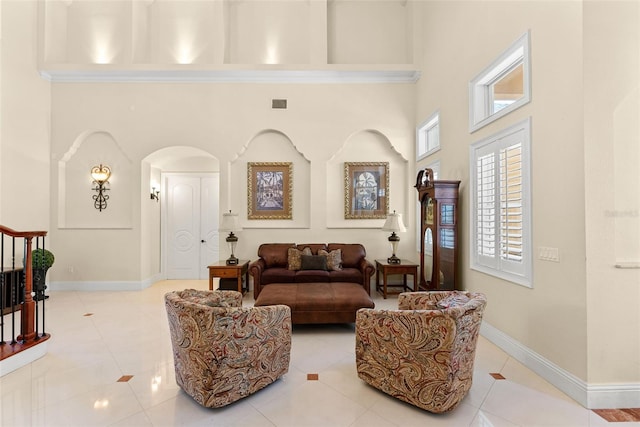 interior space featuring light tile patterned floors, baseboards, visible vents, arched walkways, and a towering ceiling