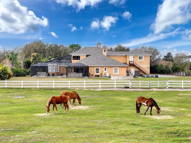 view of property's community featuring an enclosed area, a rural view, a lawn, and fence