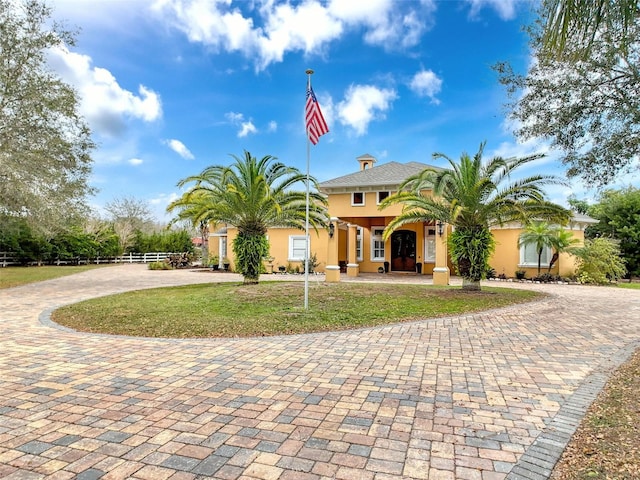 mediterranean / spanish-style house featuring driveway, fence, a front lawn, and stucco siding