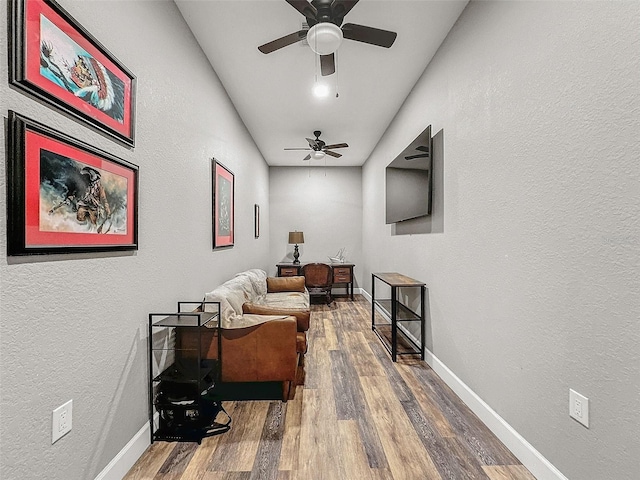 sitting room featuring a textured wall, ceiling fan, baseboards, and wood finished floors