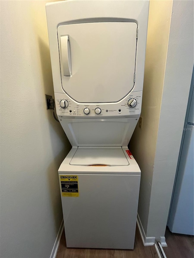 washroom featuring stacked washer / dryer, laundry area, dark wood finished floors, and baseboards