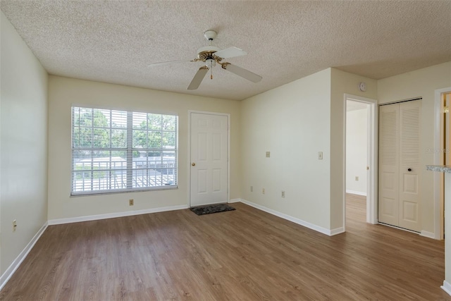 spare room with a textured ceiling, wood finished floors, and baseboards