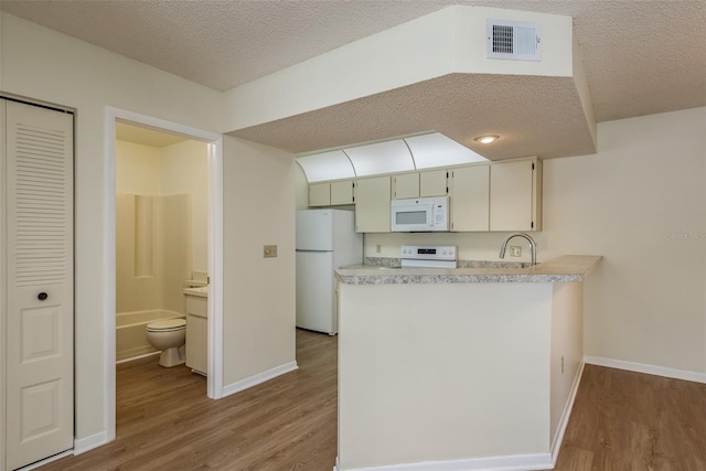 kitchen featuring white appliances, visible vents, a peninsula, light countertops, and light wood-type flooring