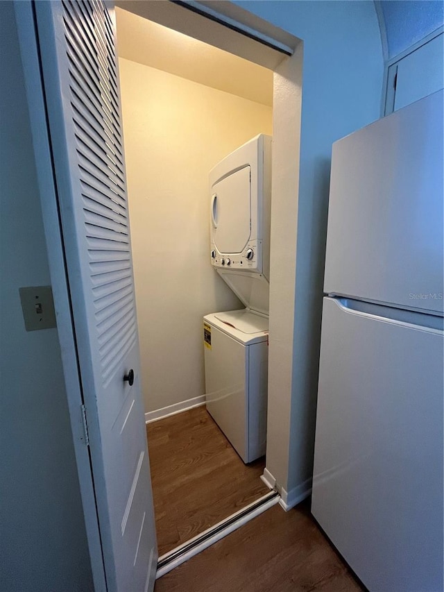 laundry area featuring stacked washer / drying machine, laundry area, dark wood finished floors, and baseboards