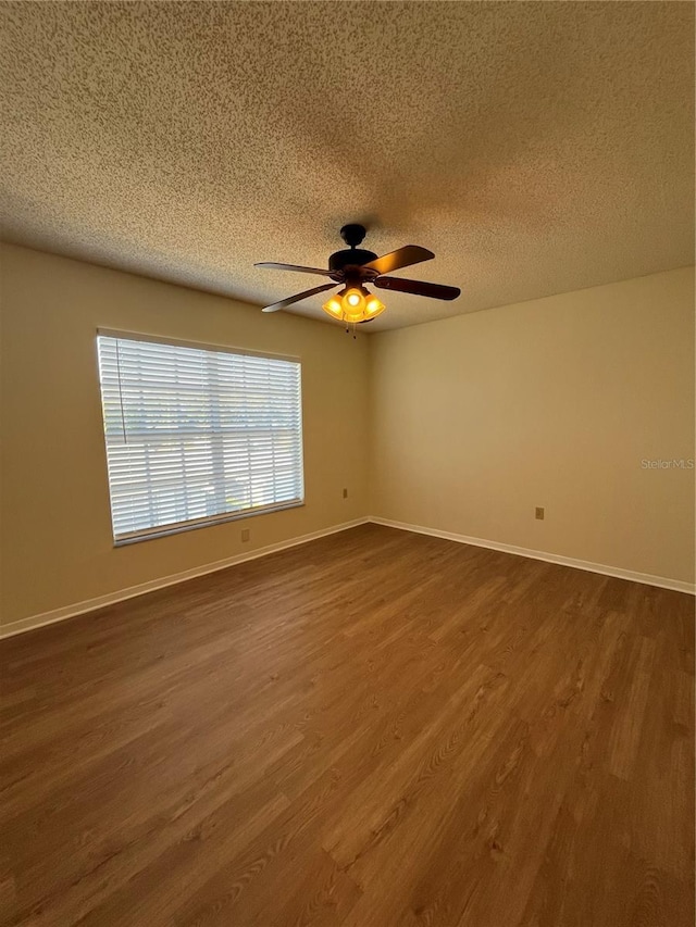 unfurnished room with a textured ceiling, dark wood-type flooring, a ceiling fan, and baseboards