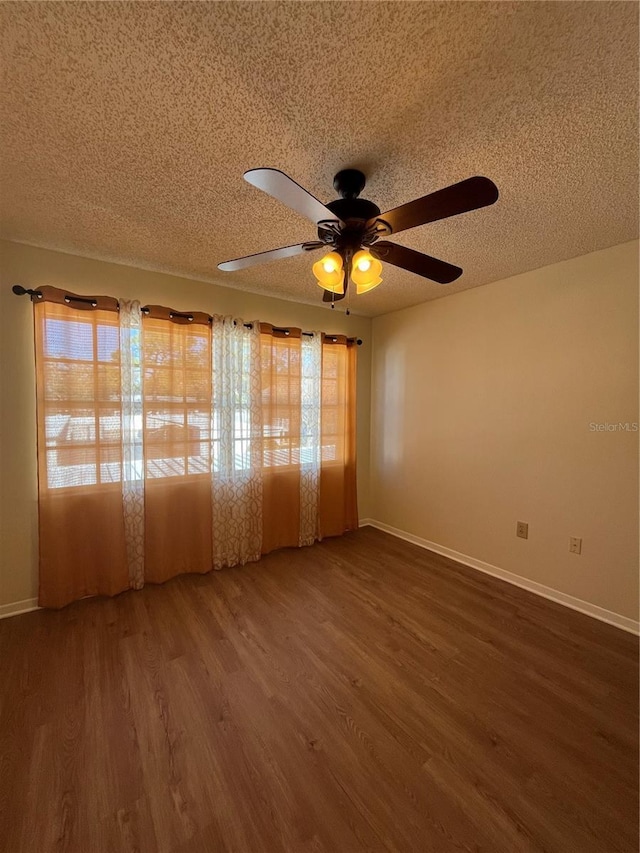 empty room with a textured ceiling, wood finished floors, and baseboards