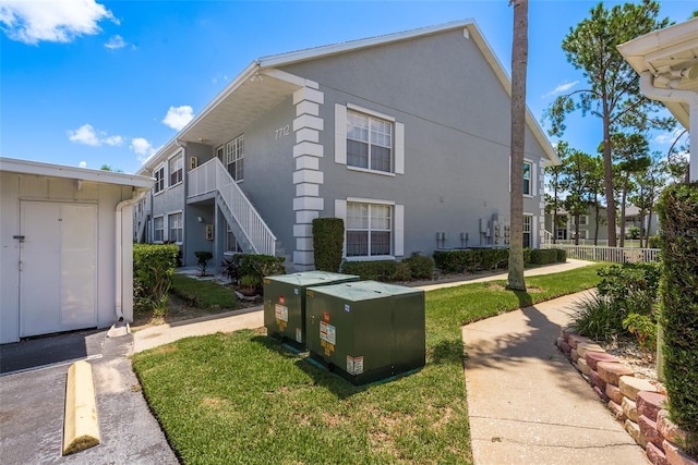 view of property exterior with stairway, a lawn, fence, and stucco siding