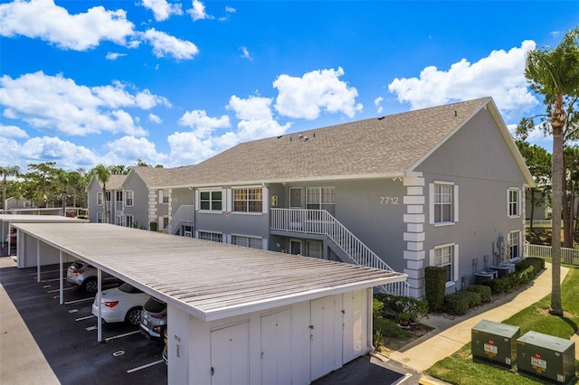 7712 Hillside Ct Unit 202, Hudson, FL 34667 - rear view of house with covered parking, stucco siding, a shingled roof, central AC unit, and stairs