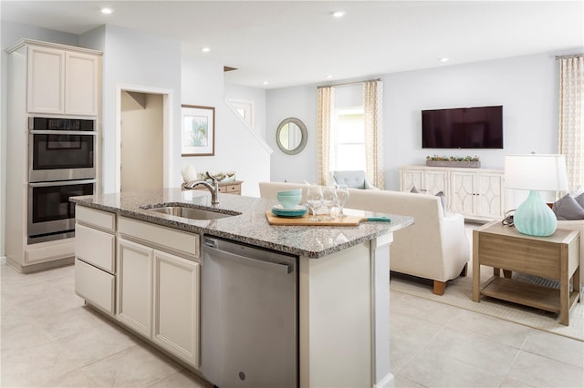 kitchen with light stone countertops, stainless steel appliances, sink, light tile patterned flooring, and a kitchen island with sink