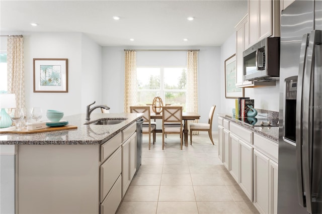 kitchen with sink, light stone countertops, appliances with stainless steel finishes, a center island with sink, and light tile patterned flooring