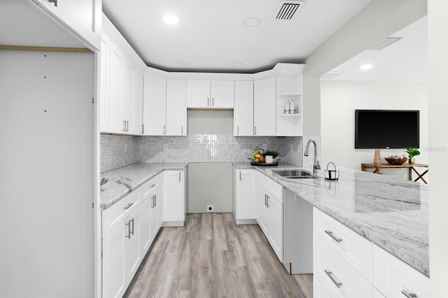 kitchen with white cabinets, light wood-type flooring, light stone countertops, sink, and tasteful backsplash