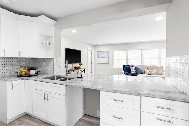 kitchen with light stone counters, light hardwood / wood-style floors, white cabinetry, sink, and decorative backsplash