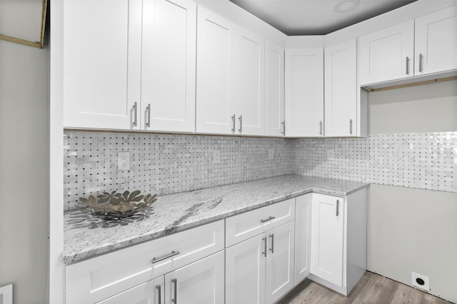 kitchen with decorative backsplash, light stone countertops, white cabinets, and light hardwood / wood-style floors