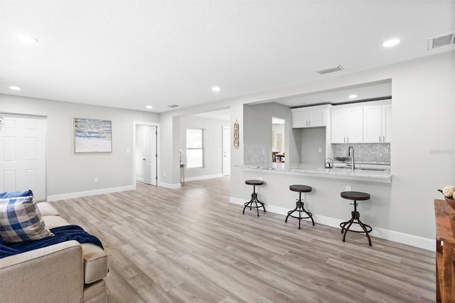 kitchen with white cabinetry, backsplash, a kitchen breakfast bar, kitchen peninsula, and light hardwood / wood-style floors