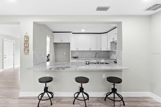 kitchen with light hardwood / wood-style flooring, white cabinets, sink, and a breakfast bar