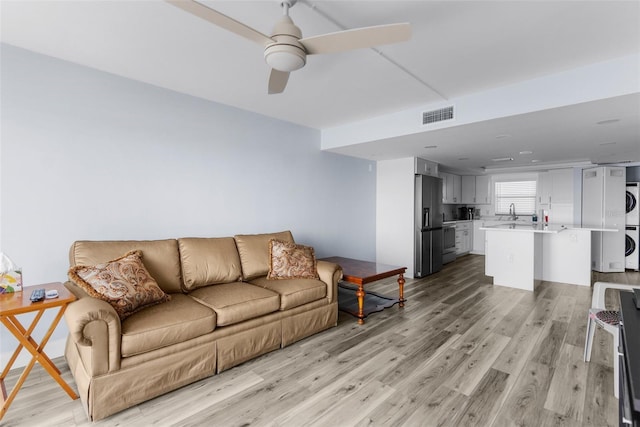 living room featuring ceiling fan, stacked washer and dryer, light hardwood / wood-style floors, and sink