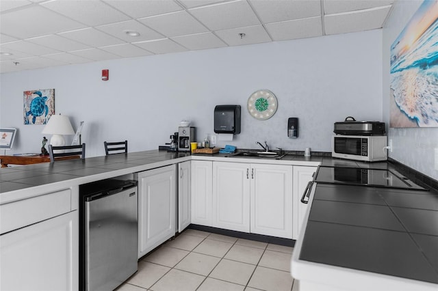 kitchen with light tile patterned floors, sink, stainless steel fridge, and white cabinetry