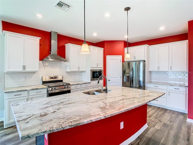 kitchen featuring visible vents, appliances with stainless steel finishes, white cabinetry, a sink, and wall chimney range hood