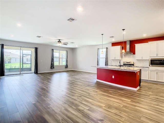kitchen featuring visible vents, appliances with stainless steel finishes, open floor plan, wall chimney range hood, and wood finished floors