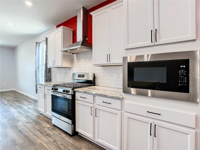 kitchen featuring built in microwave, white cabinetry, stainless steel range with gas cooktop, decorative backsplash, and wall chimney exhaust hood